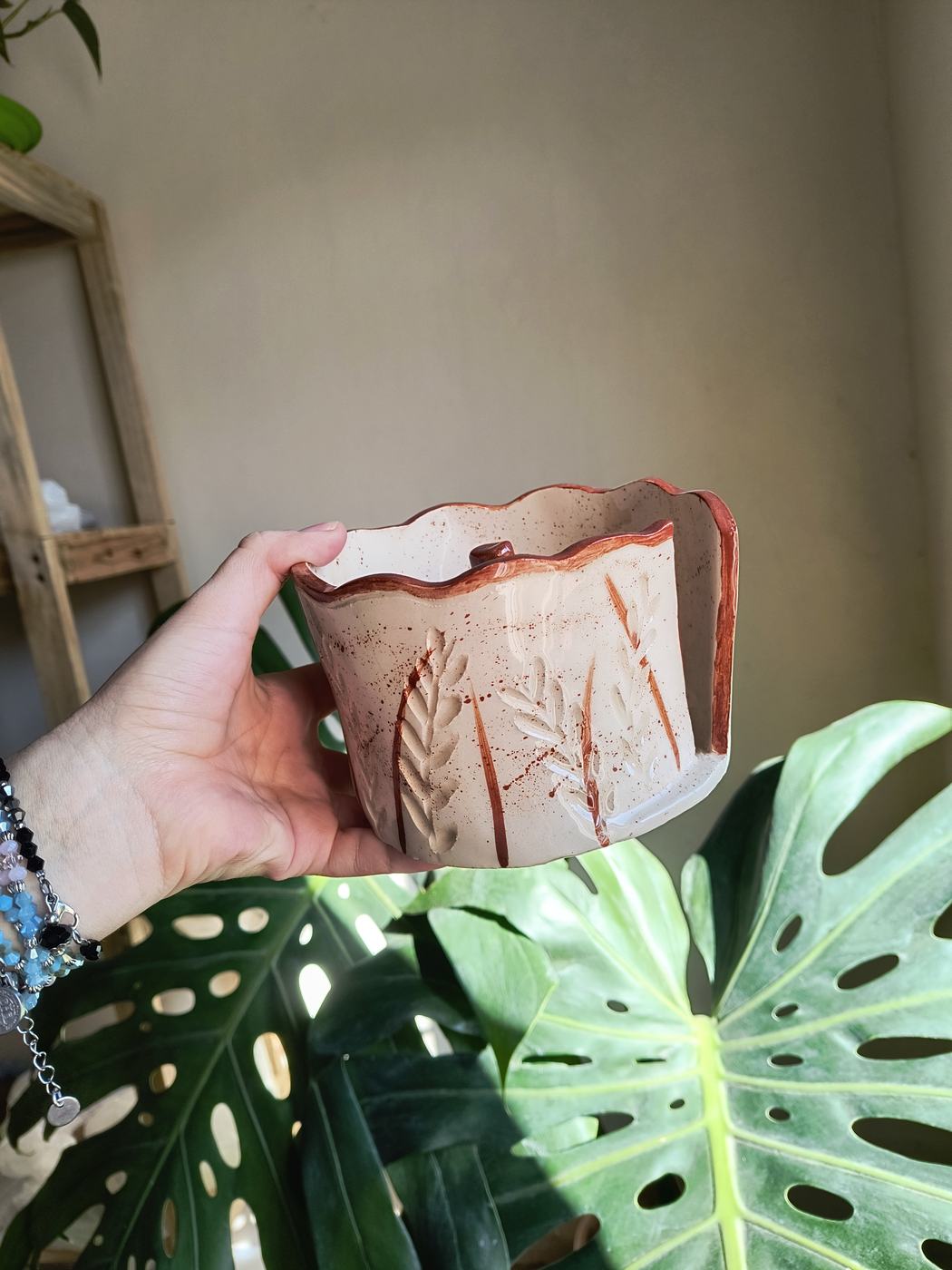 Una taza de cerámica con hojas grabadas, frente a una monstera